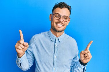 Gündelik kıyafetler ve gözlük takan genç İspanyol adam farklı yönleri gösteren kendine güvenle gülümsüyor. reklam için kopyalama alanı 