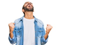 Uzun saçlı, sakallı, sıradan bir kot ceket giyen çok mutlu ve heyecanlı, kolları havada, gülümseyen ve başarı için çığlık atan çekici bir adam. kutlama konsepti. 