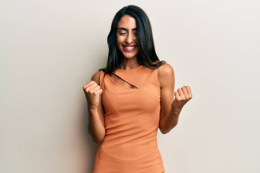 Güzel İspanyol kadın, yaz elbisesi giyiyor. Çok mutlu ve heyecanlı. Kazanan jestler yapıyor, kollarını kaldırıyor, gülümsüyor ve başarı için bağırıyor. kutlama konsepti. 