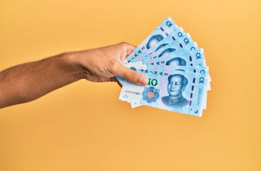 Çin malı 10 Yuan 'lık banknotları izole edilmiş sarı arka planda tutan İspanyol adamın eli..
