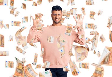 Gündelik kıyafetler giyen genç İspanyol adam on numarayı gösterip işaret ederken kendinden emin ve mutlu bir şekilde gülümsüyor..