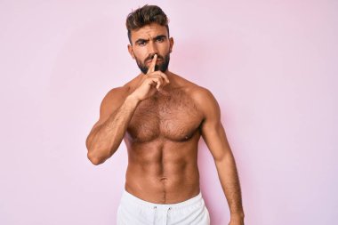 Genç İspanyol adam üstsüz duruyor ve parmakları dudaklarında sessiz olmak istiyor. sessizlik ve gizli konsept. 