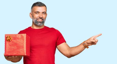 Orta yaşlı yakışıklı bir adam elinde hediyeyle gülümsüyor mutlu bir şekilde elini ve parmağını yana uzatıyordu. 