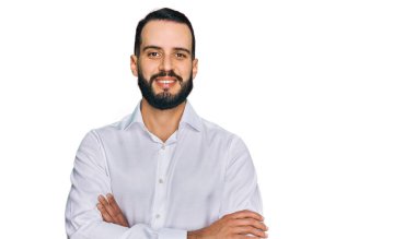 İş gömleği giyen sakallı genç adam kollarını kavuşturup kameraya bakarken gülümsüyor. pozitif kişi. 