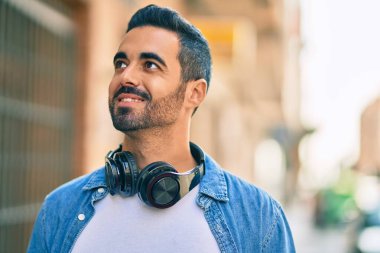 Şehirde kulaklık takarak mutlu gülümseyen genç İspanyol adam..