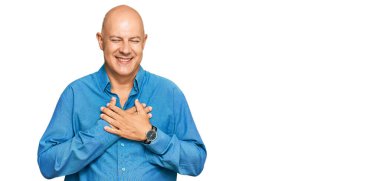 Orta yaşlı kel bir adam, sıradan kıyafetler giyiyor, elleri göğsünde, gözleri kapalı gülümsüyor ve yüzünde minnet ifadesi var. sağlık kavramı. 