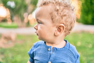 Sevimli ve mutlu küçük çocuk güneşli bir günde parkta eğleniyor. Güzel sarı saçlı erkek çocuk dışarıda oynuyor.