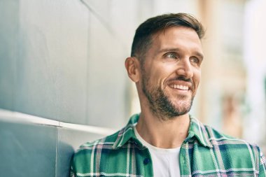 Genç beyaz adam gülümseyerek şehirde mutlu mesut duruyor..