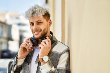 Şehirde kulaklık takarak mutlu gülümseyen genç İspanyol adam..