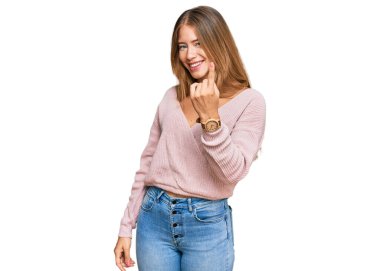 Güzel sarışın kadın, günlük kışlık pembe süveter giyiyor. Gel buraya, el kol hareketi yap. Mutlu bir şekilde karşıla ve gülümse. 
