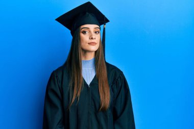 Mezuniyet şapkası ve tören cübbesi takan güzel esmer kadın yüzünde ciddi bir ifadeyle rahatlamış. Basit ve doğal bir şekilde kameraya bakıyorsun.. 
