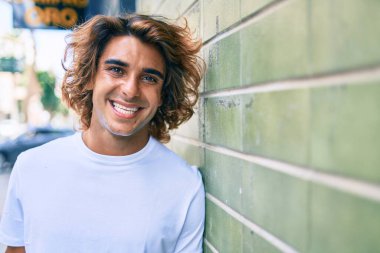 Genç yakışıklı İspanyol gülümseyen mutlu bir adam şehrin duvarına yaslanıyor.