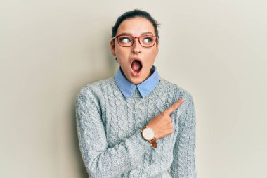 Gündelik giysiler ve gözlük takan genç beyaz kadın parmaklarını yana çevirerek şaşırdı, ağzı açık hayret içinde kaldı.. 