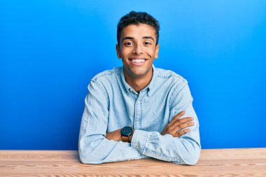 Genç, yakışıklı, Afro-Amerikalı sıradan kıyafetler giyen mutlu yüzlü, kollarını kavuşturup kameraya bakan adam. pozitif kişi. 