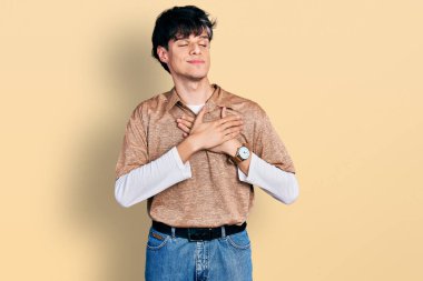 90 'lı yılların modası geçmiş yakışıklı genç adam elleri göğsünde gülümsüyor, gözleri kapalı ve yüzünde minnet ifadesi var. sağlık kavramı. 