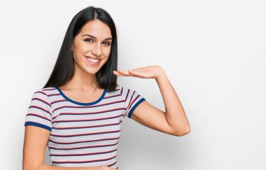 Sıradan çizgili tişört giyen genç İspanyol kız. Elleriyle büyük ve büyük bir işaret, ölçü sembolü gösteriyor. Kameraya bakıp gülümsüyor. ölçüm kavramı. 