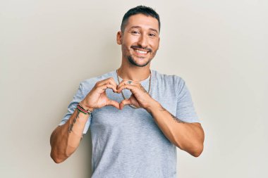 90 'lı yılların tarzında dövmeleri olan yakışıklı bir adam. Aşkta gülümseyen altın bir zincir. Elleriyle kalp sembolü çiziyor. romantik kavram. 