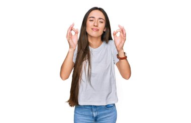 Günlük beyaz tişört giyen, gözleri kapalı gülümseyen genç İspanyol kız parmaklarıyla meditasyon hareketi yapıyor. yoga konsepti. 
