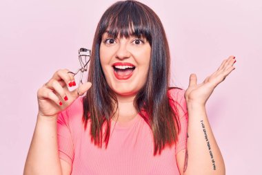 Kirpik bigudiyle zaferi kutlayan genç ve cüsseli bir kadın. Gülümseyen bir gülümseme ve ellerini kaldırarak kazanan bir ifade. 