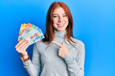 Elinde İsviçre frangı banknotları tutan genç kızıl saçlı kız mutlu bir şekilde elini ve parmağını gösterdi. 