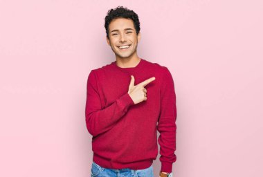 Genç, yakışıklı, günlük kıyafetler giyen, neşeli, yüzünde bir gülümseme olan, mutlu ve doğal bir ifadeyle elini ve parmağını kaldıran bir adam. 