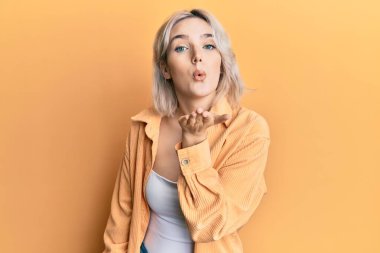 Gündelik kıyafetler giyen genç sarışın kız kameraya bakıyor ve havada bir öpücük savuruyor. Güzel ve seksi. aşk ifadesi. 