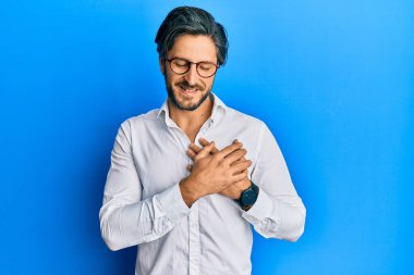 Gündelik kıyafetler ve gözlük takan genç İspanyol adam elleri göğsünde, gözleri kapalı gülümsüyor ve yüzünde minnet ifadesi var. sağlık kavramı. 
