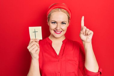 Elinde Katolik haçı tutan genç sarışın kadın bir fikir ya da soruyla şaşırdı. 