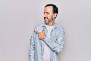 Orta yaşlı, sıradan bir kot gömlek giyen yakışıklı bir adam izole edilmiş beyaz arka planda dikiliyor. Gülümsüyor, eli ve parmağı yana doğru uzanıyor.