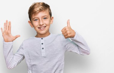 Kafkasyalı küçük çocuk gündelik kıyafetler giyip altı numaralı parmaklarıyla işaret ederken kendinden emin ve mutlu bir şekilde gülümsüyor.. 