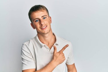 Beyaz polo giyen, neşeli gülümseyen, eli ve parmağı yanda genç beyaz bir adam. 