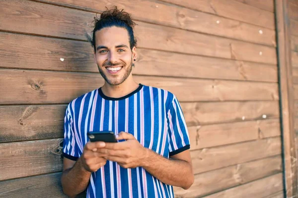 Joven Hombre Hispano Sonriendo Feliz Usando Smartphone Apoyado Pared —  Fotos de Stock
