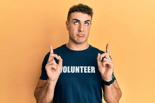 Jovem Hispânico Vestindo Camiseta Voluntária Apontando Para Cima Parecendo Triste — Fotografia de Stock