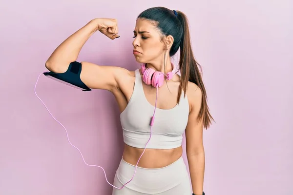 ジムの服を着て腕の筋肉を示すヘッドフォンの強い人を使用して若いヒスパニック女性 自信と力の誇り — ストック写真