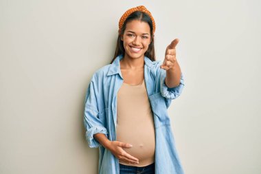 Güzel İspanyol bir kadın bebek bekliyor, hamile karnına dokunuyor gülümseyerek dostça el sıkışarak selam veriyor. başarılı iş. 