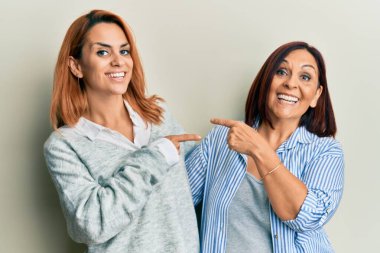 Latin anne ve kız günlük kıyafetler giyip gülümsüyor ve mutlu bir şekilde el ve parmak gösteriyorlar. 