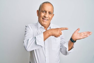 Yakışıklı, beyaz gömlekli adam kameraya hayret ediyor ve gülümsüyor. Elinle ve parmağınla işaret ediyor.. 