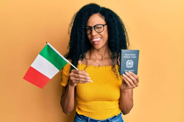 Orta yaşlı Afro-Amerikalı kadın elinde İtalyan bayrağı ve pasaportuyla kameraya bakıyor. Seksi bir ifadeyle, neşeli ve mutlu bir yüzle.. 