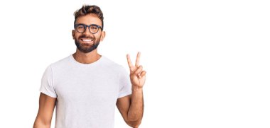 Gündelik kıyafetler giyen ve gözlüklü genç İspanyol adam iki numarayı gösterip işaret ederken kendinden emin ve mutlu bir şekilde gülümsüyor.. 