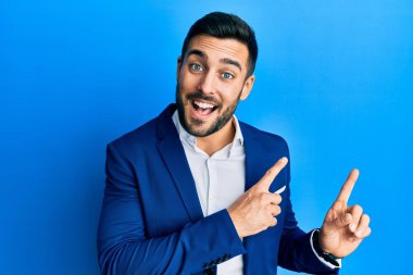 Genç İspanyol iş adamı iş ceketi giyiyor gülümsüyor ve kameraya bakıyor iki eliyle ve parmaklarıyla kenarı işaret ediyor.. 