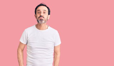 Sıradan tişörtler giyen, komik suratlı, yanakları şişen orta yaşlı yakışıklı bir adam. Havayla şişmiş ağız, çılgın bir ifade.. 