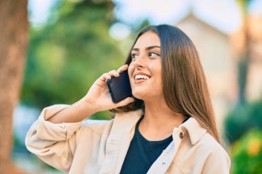 Genç İspanyol kız gülümsüyor. Parktaki akıllı telefondan konuşarak mutlu oluyor..