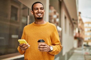 Genç Afrikalı Amerikalı adam akıllı telefon kullanıyor. Şehirde kahve içiyor..