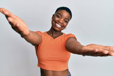 Sıradan turuncu tişörtler giyen Afro-Amerikalı genç bir kadın sarılmak için kollarını açmış kameraya bakıyor. Mutluluğu kucaklayan neşeli bir ifade.. 