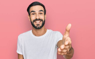 Latin asıllı genç bir adam, günlük beyaz tişörtler giyip dostça bir şekilde el sıkışarak selamlıyor ve hoş geldin diyor. başarılı iş. 