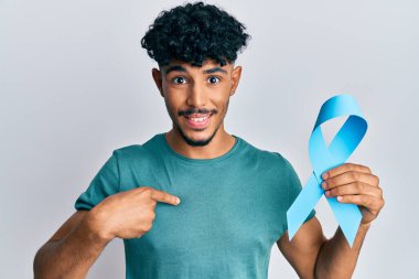 Genç Arap yakışıklı adam mavi kurdele tutuyor mutlu ve gururlu bir kendini işaret ediyor. 