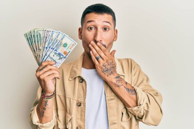 Dövmeleri olan yakışıklı bir adam. Dolarları elinde tutan ağzı ağızla kaplayan, şok olan ve hata yapmaktan korkan biri. şaşırmış ifade 