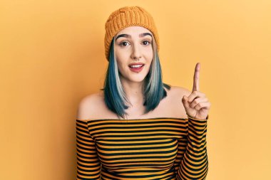 Yün şapka takan genç ve modern bir kız başarılı bir fikri işaret ediyor. Heyecanlı ve mutlu. Bir numara.. 