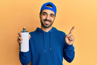 Süveter giyen genç İspanyol adam elinde grafiti spreyi ile gülümsüyor. 