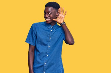 Genç Afro-Amerikan bir adam, günlük giysiler giymiş, ağzı kulaklarına varan bir gülümsemeyle dedikodu ve söylentileri dinliyor. Sağırlık kavramı. 